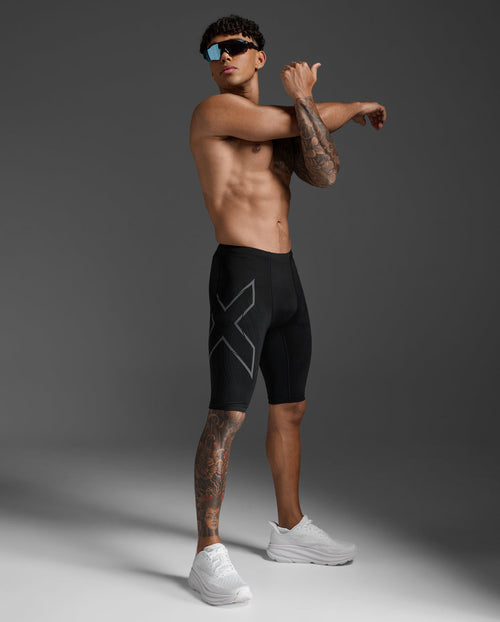 Male athlete wearing the 2XU Light Speed Compression Shorts in Black/Black Reflective, stretching pose showing the thigh X logo.