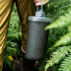 Action shot of cyclist reaching for Hydrapak bottle on trail quick access hydration.

