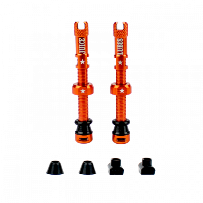 A pair of orange Juice Lubes tubeless valves (65mm) with their caps on, showcasing the vibrant color and sleek design against a clean background.

