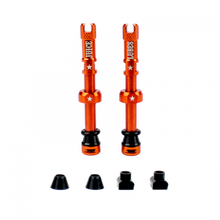 A pair of orange Juice Lubes tubeless valves (65mm) with their caps on, showcasing the vibrant color and sleek design against a clean background.

