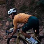 A male cyclist in a brown jersey and dark cycling shorts rides a gravel bike, showcasing a Magicshine SEEMEE 50 V2.0 smart rear light