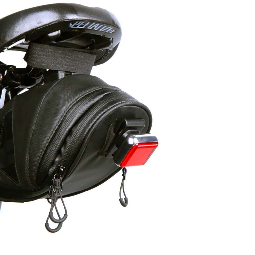  A rectangular Magicshine rear light with a red glowing LED strip, clipped vertically onto a black backpack with molle webbing