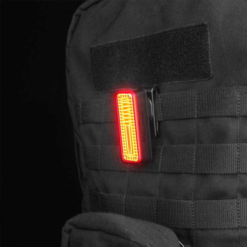 A Magicshine SEEMEE rear light clipped onto a black backpack strap, with the red light illuminated.