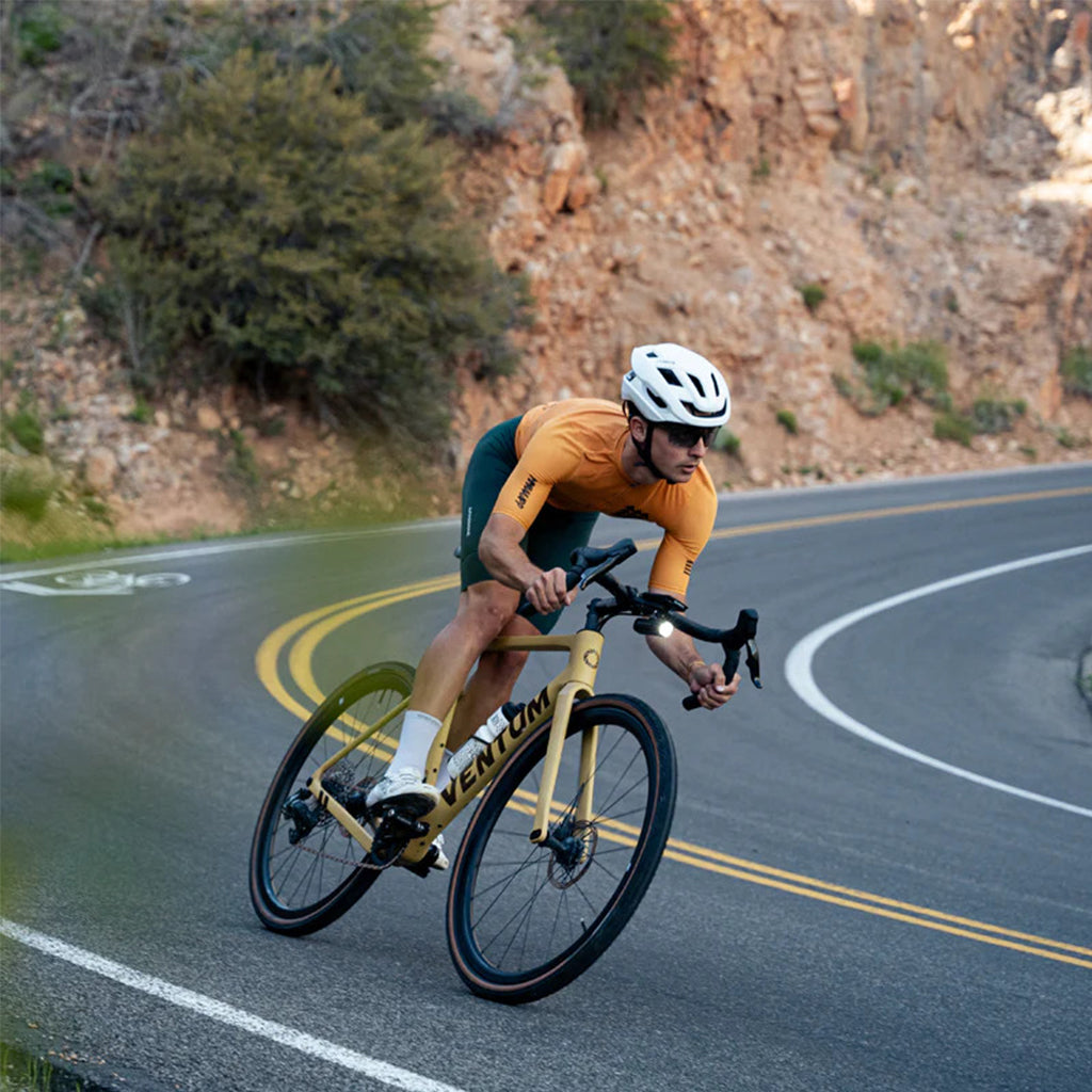 A close-up of a Magicshine ALLTY 1200U underneath-mounted bike light and a Garmin computer on a bicycle handlebar.