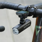  "A Magicshine ALLTY 1200U bike light mounted underneath a bicycle handlebar, beneath a Garmin cycling computer, indicating an integrated setup for improved aesthetics and light positioning.