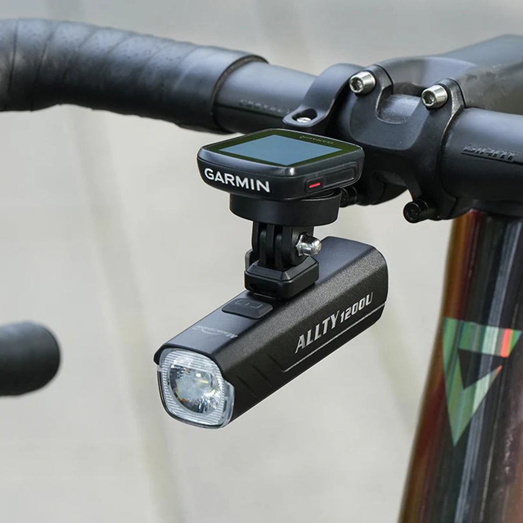  "A Magicshine ALLTY 1200U bike light mounted underneath a bicycle handlebar, beneath a Garmin cycling computer, indicating an integrated setup for improved aesthetics and light positioning.