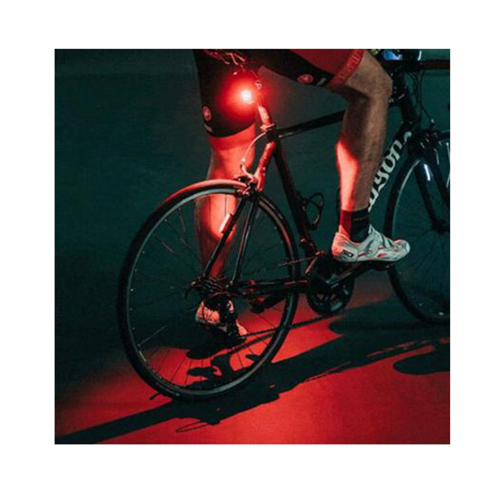 Close-up of a Magicshine SEEMEE 200 V3.0 smart rear bike light illuminating the ground beneath a cyclist's road bike