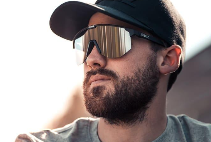A man models Bliz Hero Black Sport Sportglasses, wearing a black top and stylish sunglasses