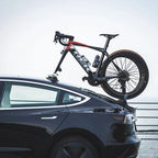 A bicycle rests on top of a car, showcasing the TreeFrog Pro 2 Bike Rack designed for road and mountain bikes