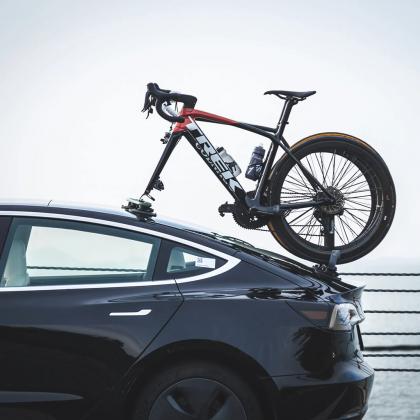 A bicycle rests on top of a car, showcasing the TreeFrog Pro 2 Bike Rack designed for road and mountain bikes
