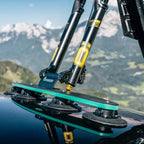 A bicycle on a car's roof with mountains behind, highlighting the Tree Frog Thru Axle Fork Mount for cycling enthusiasts