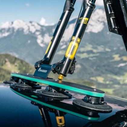 A bicycle on a car's roof with mountains behind, highlighting the Tree Frog Thru Axle Fork Mount for cycling enthusiasts