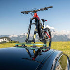 A bicycle rests atop a car, with majestic mountains in the background, showcasing the Tree Frog Thru Axle Fork Mount
