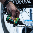 Blub Ceramic Lube 120ml bottle held over a bicycle chain and disc rotor during application.
