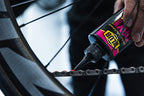 Hand applying Blub Dry Lube to a bicycle chain near the rear wheel.