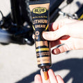 Blub Lithium Grease 100g tube being squeezed by hand next to a bicycle wheel and hub.