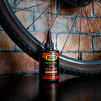 Blub Tire Sealant 120ml bottle standing beside a mountain bike wheel and tire against a brick wall.