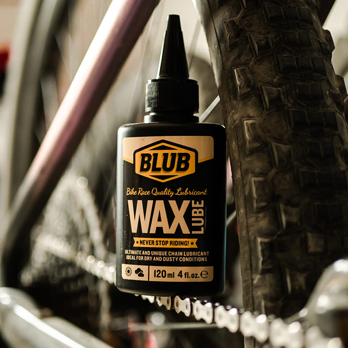 Blub Wax Lube 120ml bottle mounted on a bike frame near the chain and a knobby MTB tire.