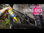 Juice Lubes Viking Juice - All Condition Chain Oil (130ml), shown being applied to a bike chain, indicating its adaptability for year-round riding.