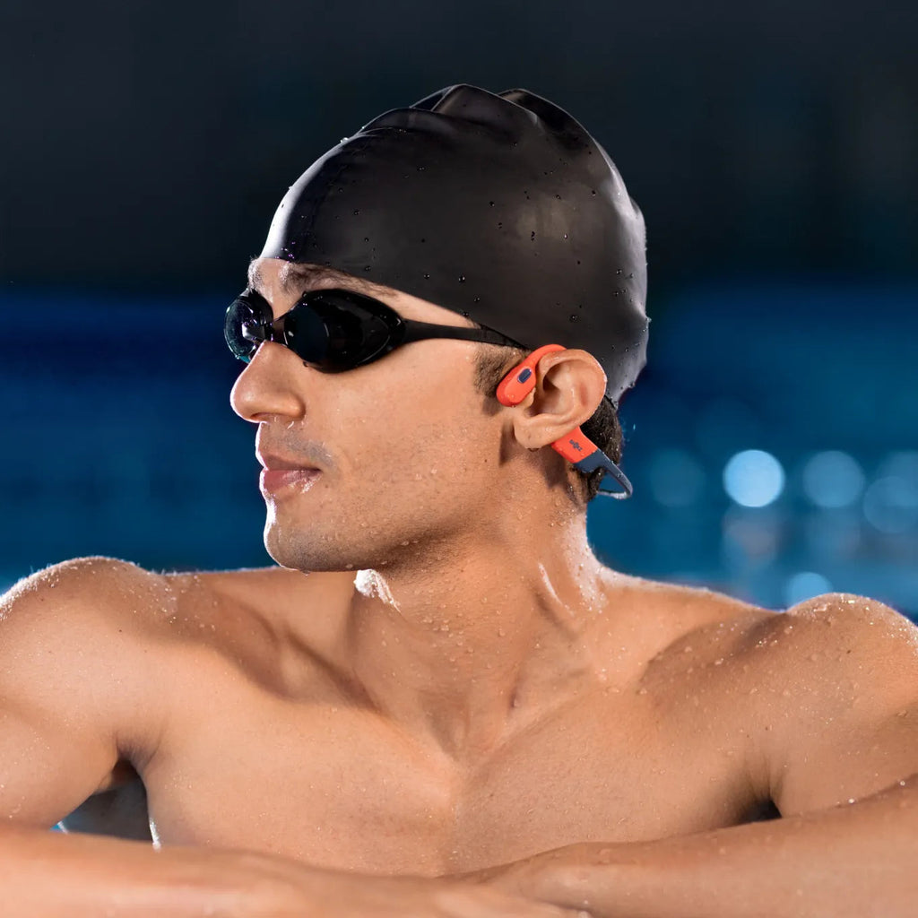 Swimmer wearing Shokz OpenSwim Pro red waterproof headphones in open water